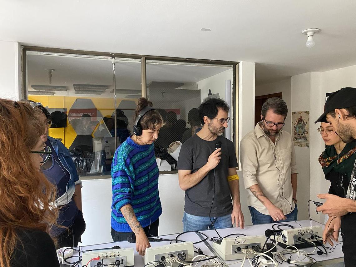 Varias personas están paradas en torno a una mesa con equipos de interpretación. Una de ellas habla en el micrófono y las otras miran y escuchan.